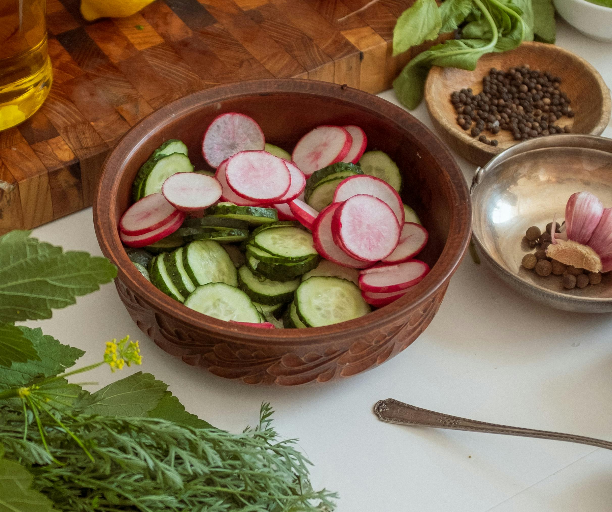Wooden bowl filled with fresh sliced cucumbers and radishes, surrounded by herbs and spices, perfect for healthy meals.