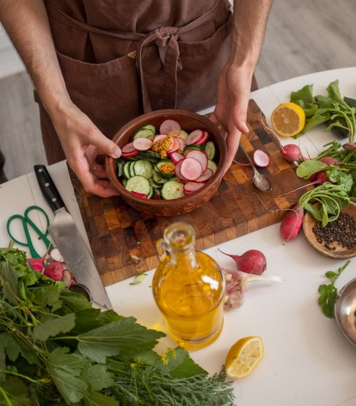 Free Chef prepares a fresh vegetable salad with radishes, cucumbers, and olive oil on a wooden board. Stock Photo