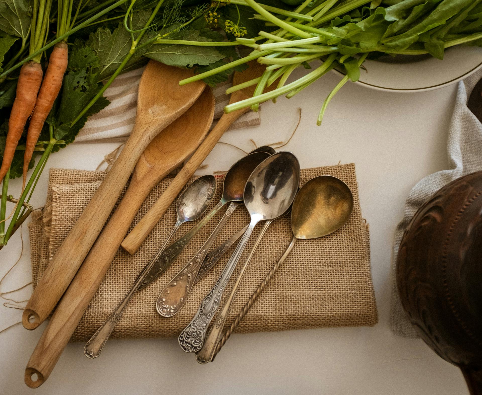 A rustic display of vintage spoons on burlap surrounded by fresh vegetables, creating a cozy kitchen atmosphere.