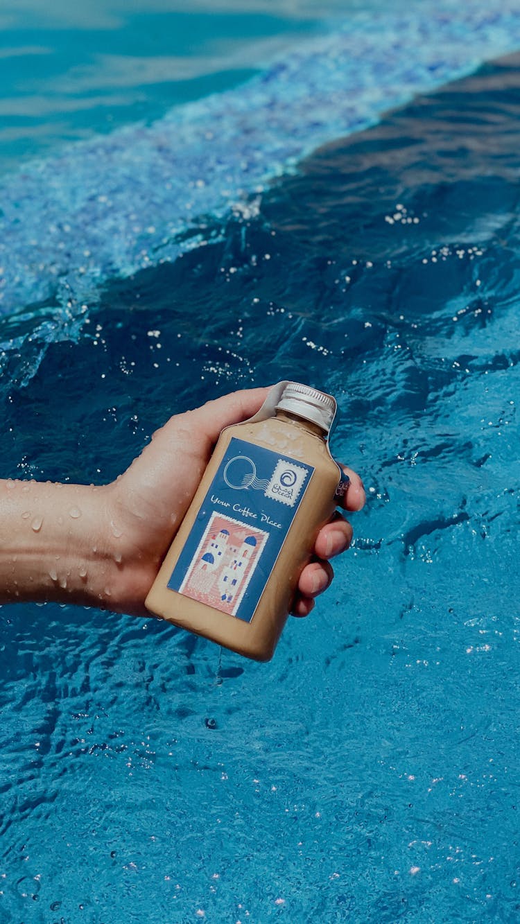 Person Holding Labeled Bottle Near A Body Of Water