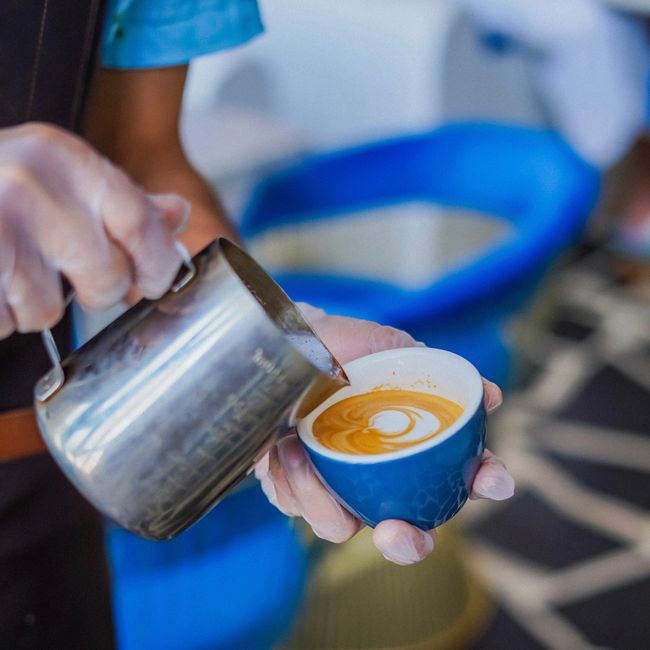 Close-up of a barista creating latte art in a blue cup with precision pouring technique. - 7 Must-Visit Coffee Shops and Cafes in Bridgetown