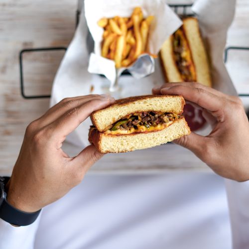 Free A person holding a sandwich with a filling of cheese and meat, accompanied by crispy french fries. Stock Photo