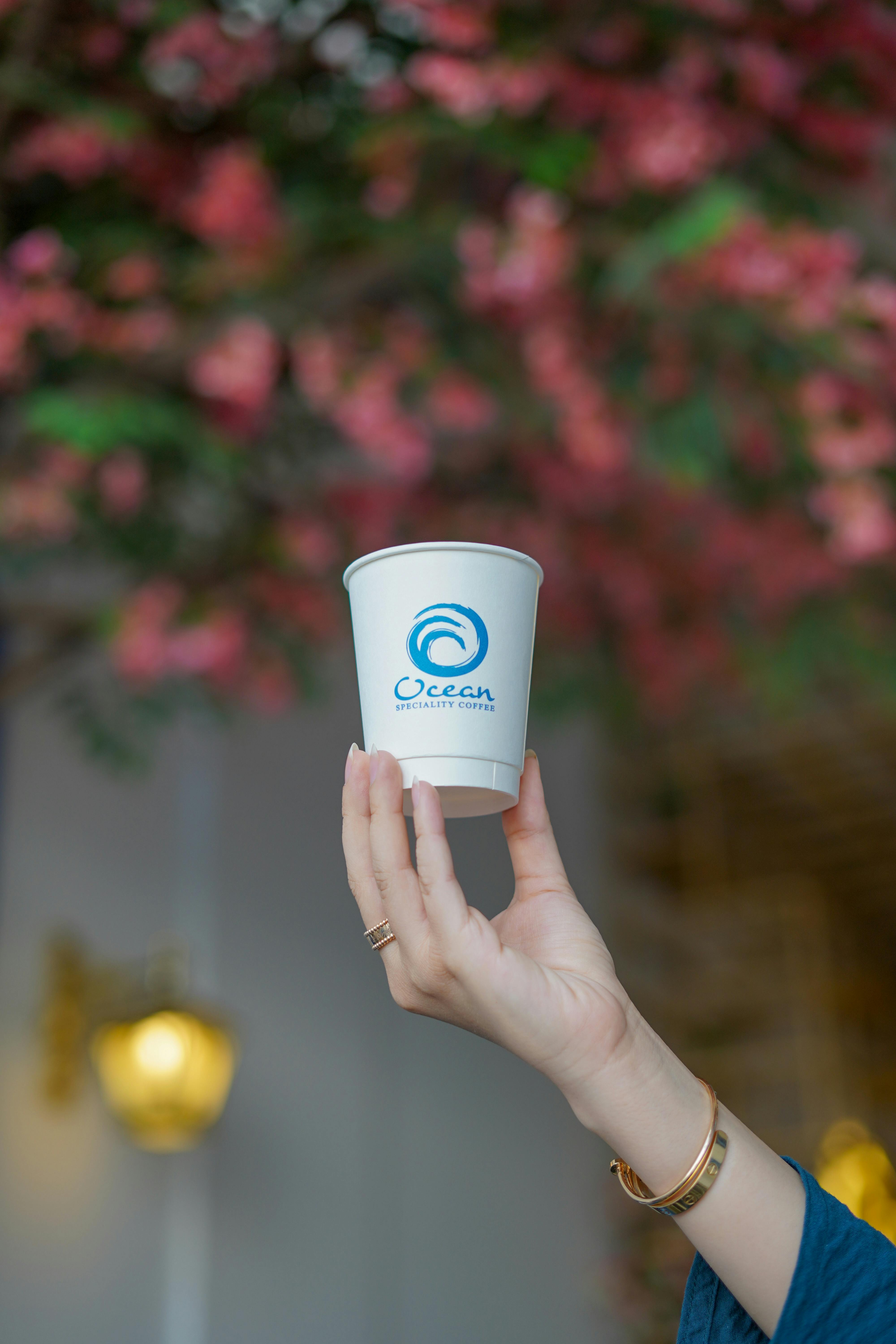 A stylish hand holds a branded cup against a vibrant floral backdrop, highlighting branding.