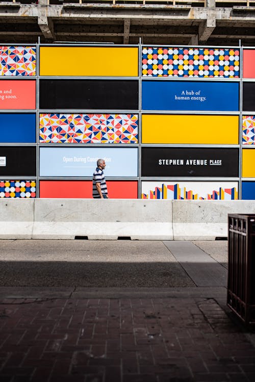 A Man Walking Near the Colorful Wall on the Roadside