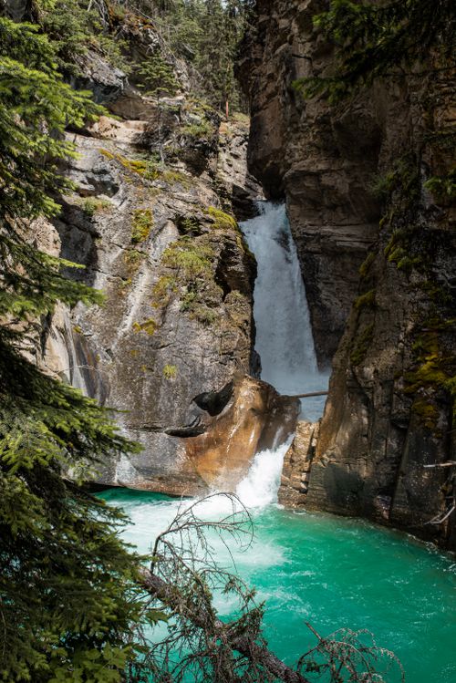 Free Majestic waterfall cascading down rugged cliffs into a turquoise river surrounded by forest. Stock Photo