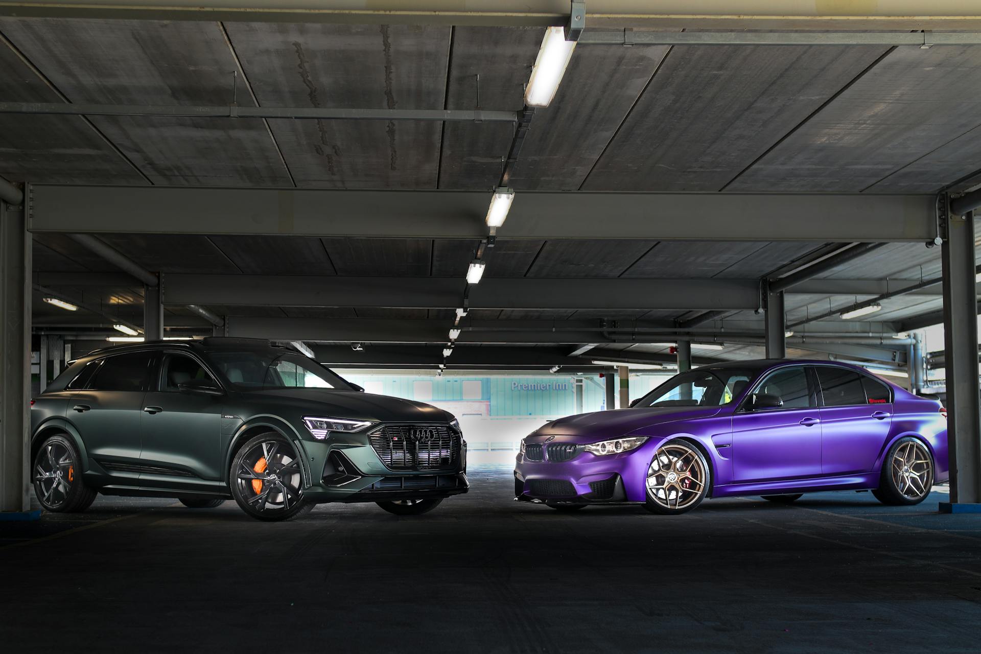 Two luxury vehicles, an Audi E-tron and a BMW, showcased in an indoor parking garage.