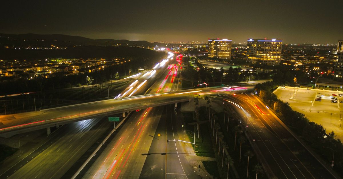 Aerial view of a bustling city highway at night, showcasing vibrant lights and urban architecture.