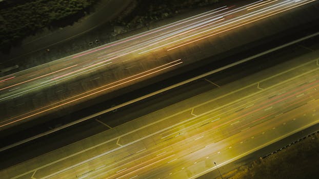 Aerial long exposure of highway showcasing light trails from moving vehicles at night.
