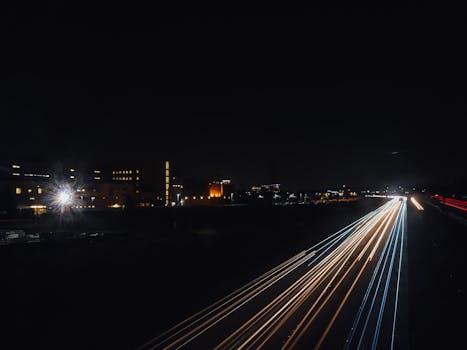 Nighttime cityscape featuring dynamic light trails across a bustling urban road.