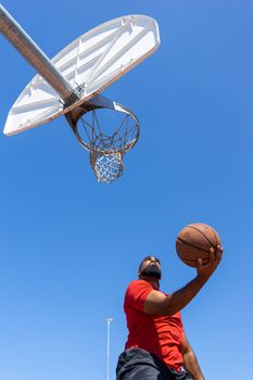 Man playing basketball outdoors with a clear blue sky backdrop.