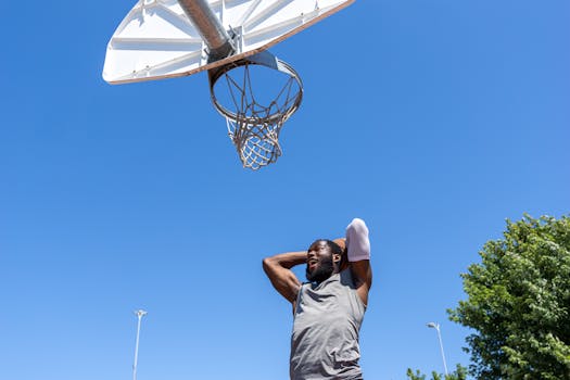 A thrilling action shot of a man dunking on an outdoor basketball court under a clear blue sky.