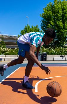 Athletic male playing basketball, showcasing skills on an outdoor court under blue skies.