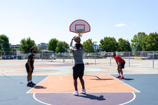 Three men playing basketball on an outdoor court under a clear sky, enjoying a friendly game.