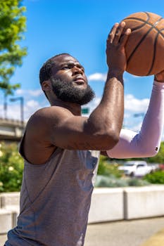 Athletic man practicing basketball shooting outdoors under a clear blue sky.
