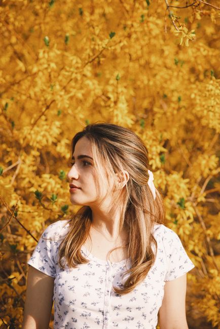 A woman gazes thoughtfully surrounded by vibrant yellow autumn foliage.