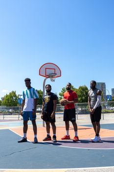 Four men standing on an outdoor basketball court under a clear sky, ready to play.