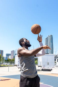 Athlete in sleeveless shirt skillfully spinning basketball outdoors with modern cityscape.