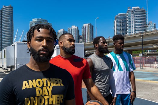 A group of four young men standing on an outdoor basketball court with city skyscrapers in the background.