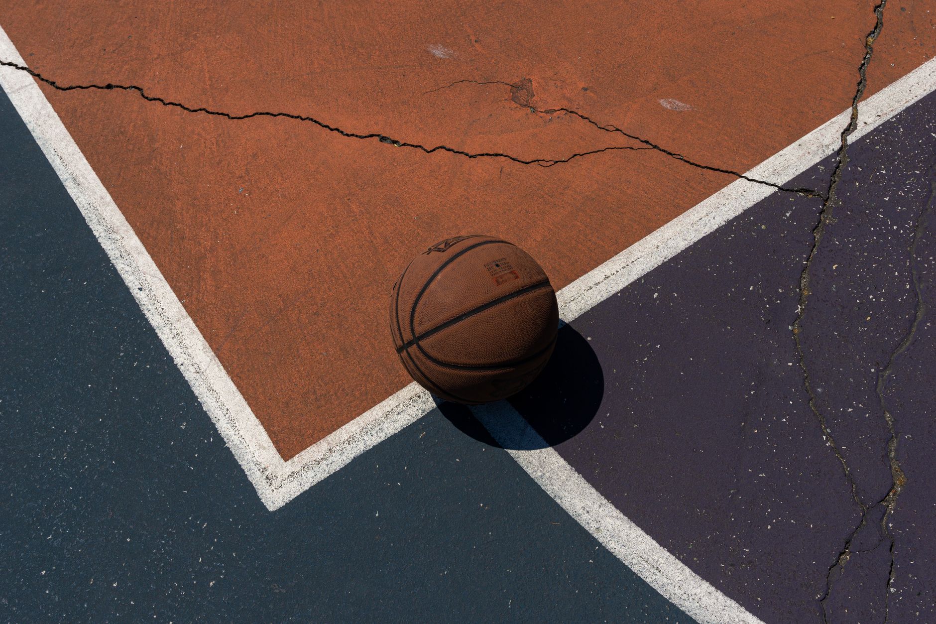 A lone basketball rests on a cracked outdoor court, emphasizing urban sport aesthetics.