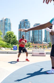 Two men playing basketball on an outdoor court with skyscrapers in the background.