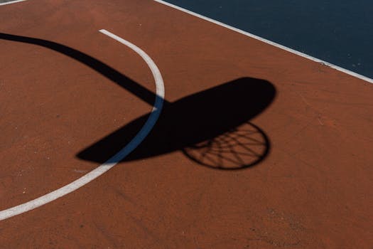 Shadow of a basketball hoop on an outdoor court during the day.