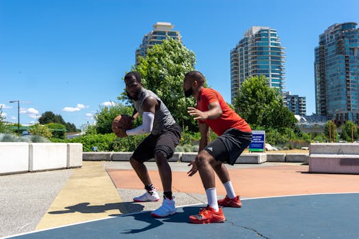 Two men playing basketball on an outdoor court with city skyline in the background.