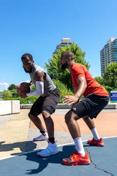 Two men playing basketball on an outdoor court in summer, showcasing sportsmanship and skill.