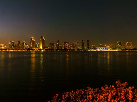Capture of an illuminated city skyline reflecting on water under a dark sky at night.