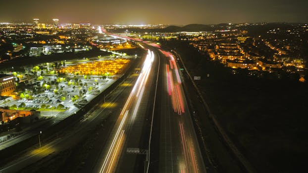 Aerial view of a vibrant city expressway at night with moving car light trails and illuminated surroundings.