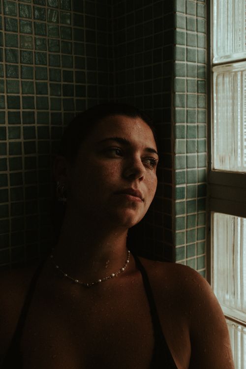 Free A thoughtful woman leaning against a tiled wall indoors, in soft lighting. Stock Photo
