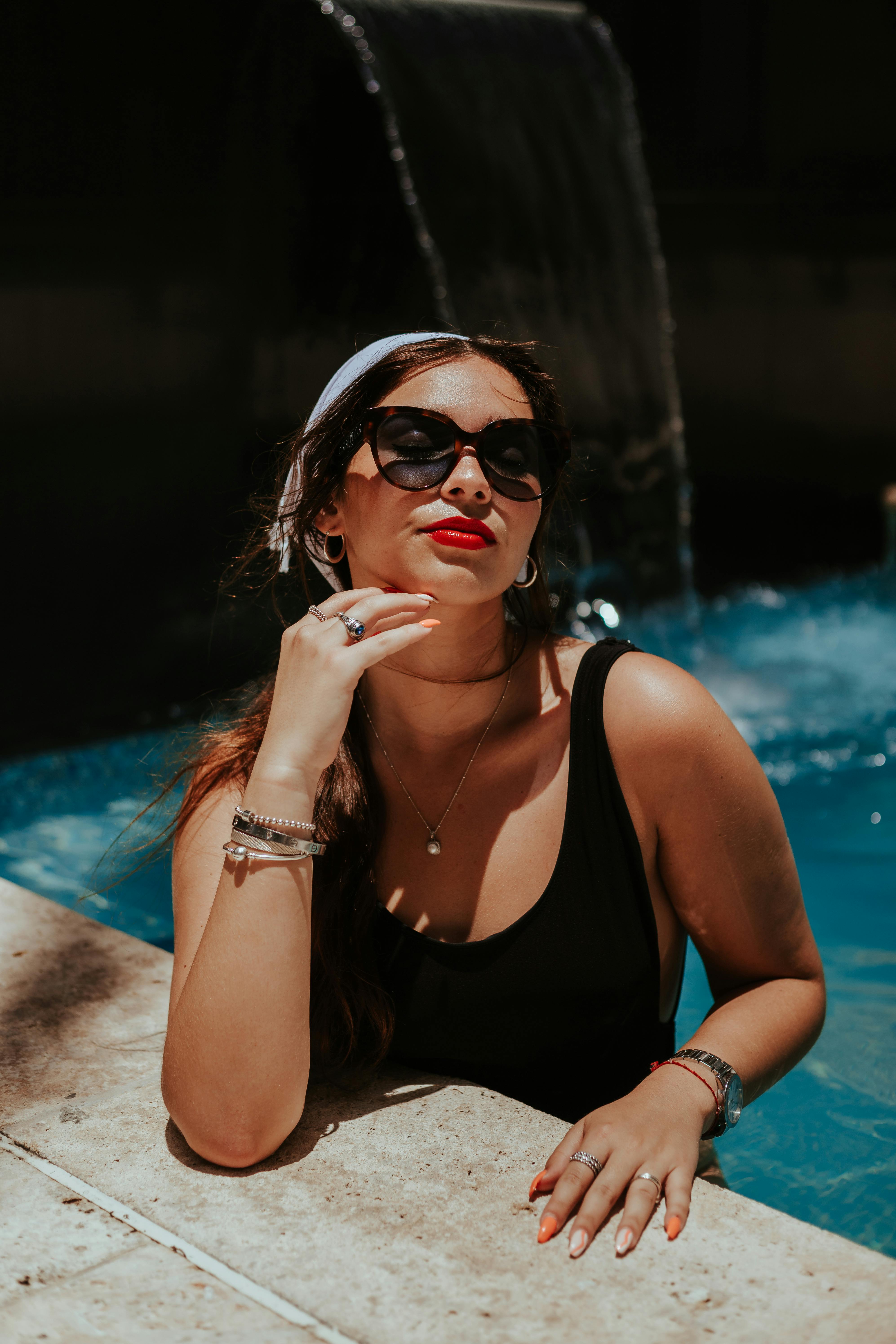 Glamorous woman with sunglasses poses by a pool, exuding summer vibes.