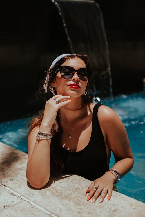 Woman in Black Swimsuit Wearing Sunglasses while Posing at the Camera