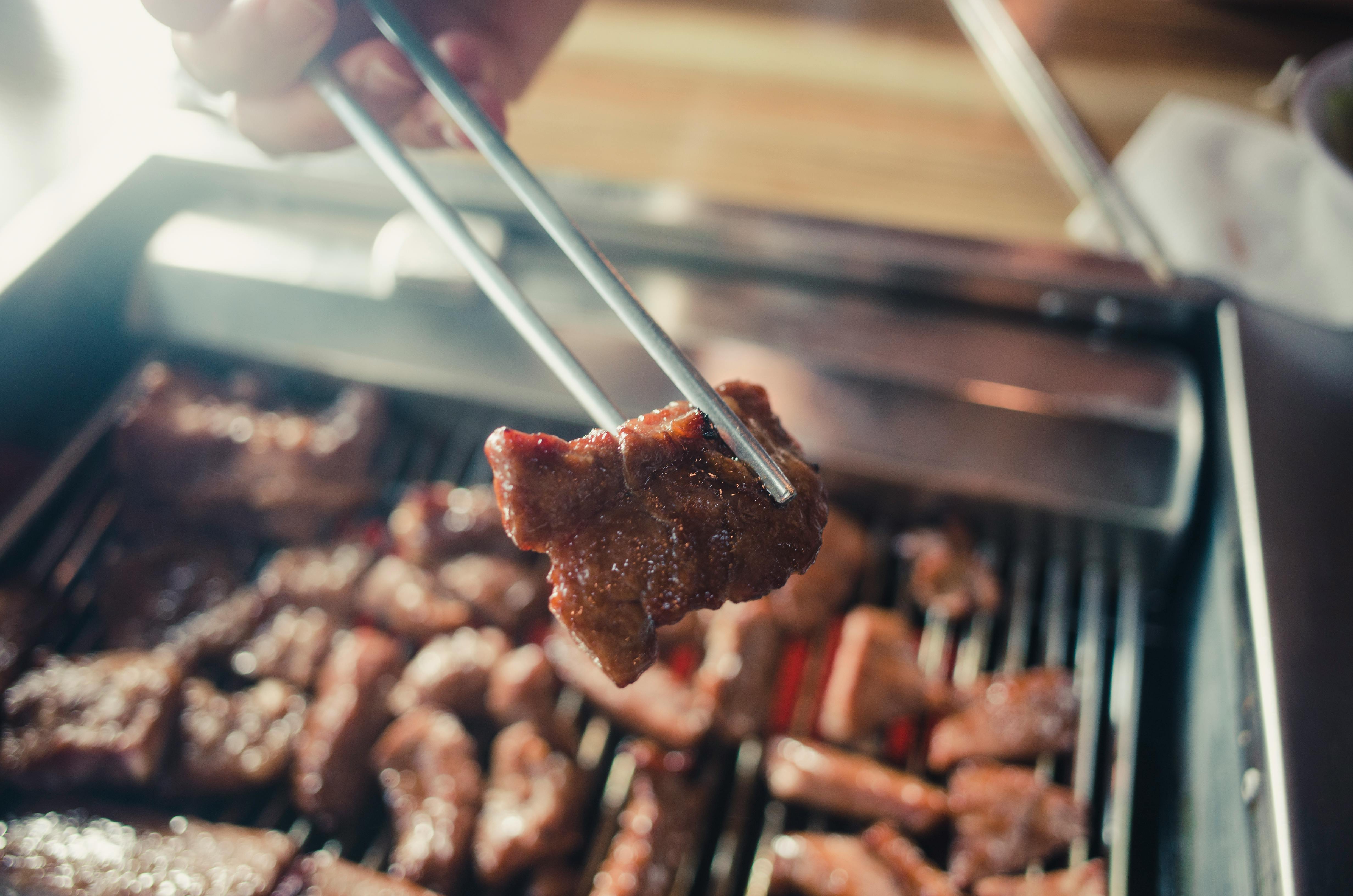 Juicy meat being grilled on a barbecue, captured close-up with chopsticks.