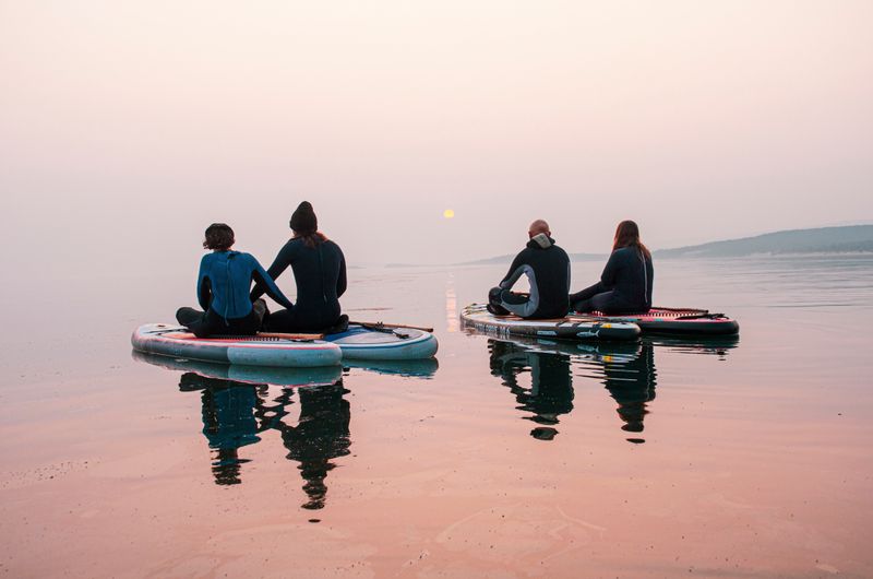Grupo remando en paddle surf con el sol bajo sobre el mar en calma