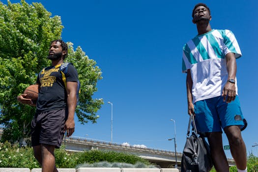 Two men with sportswear walk outdoors in summer, one with a basketball.