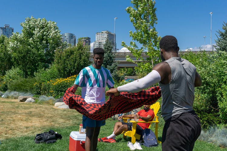 Men In Sportswear Laying Out A Picnic Blanket At A Park