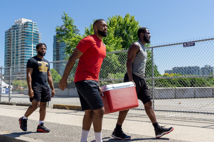 Men In Sportswear Carrying A Cooler While Walking