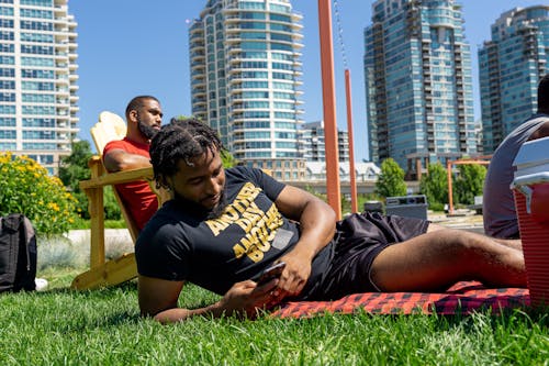 Man in Black Shirt Lying Down on Grass while Using His Smartphone