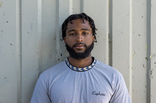 Bearded Man in Gray Shirt Looking at Camera beside the Gray Wall