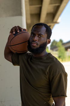 Athletic African American man with beard holding basketball under bridge in urban setting.