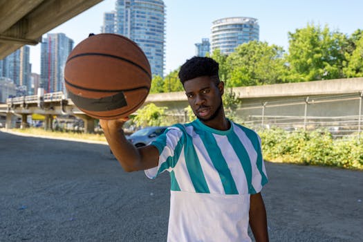 Man holding a basketball under a city bridge, showcasing athleticism and style.