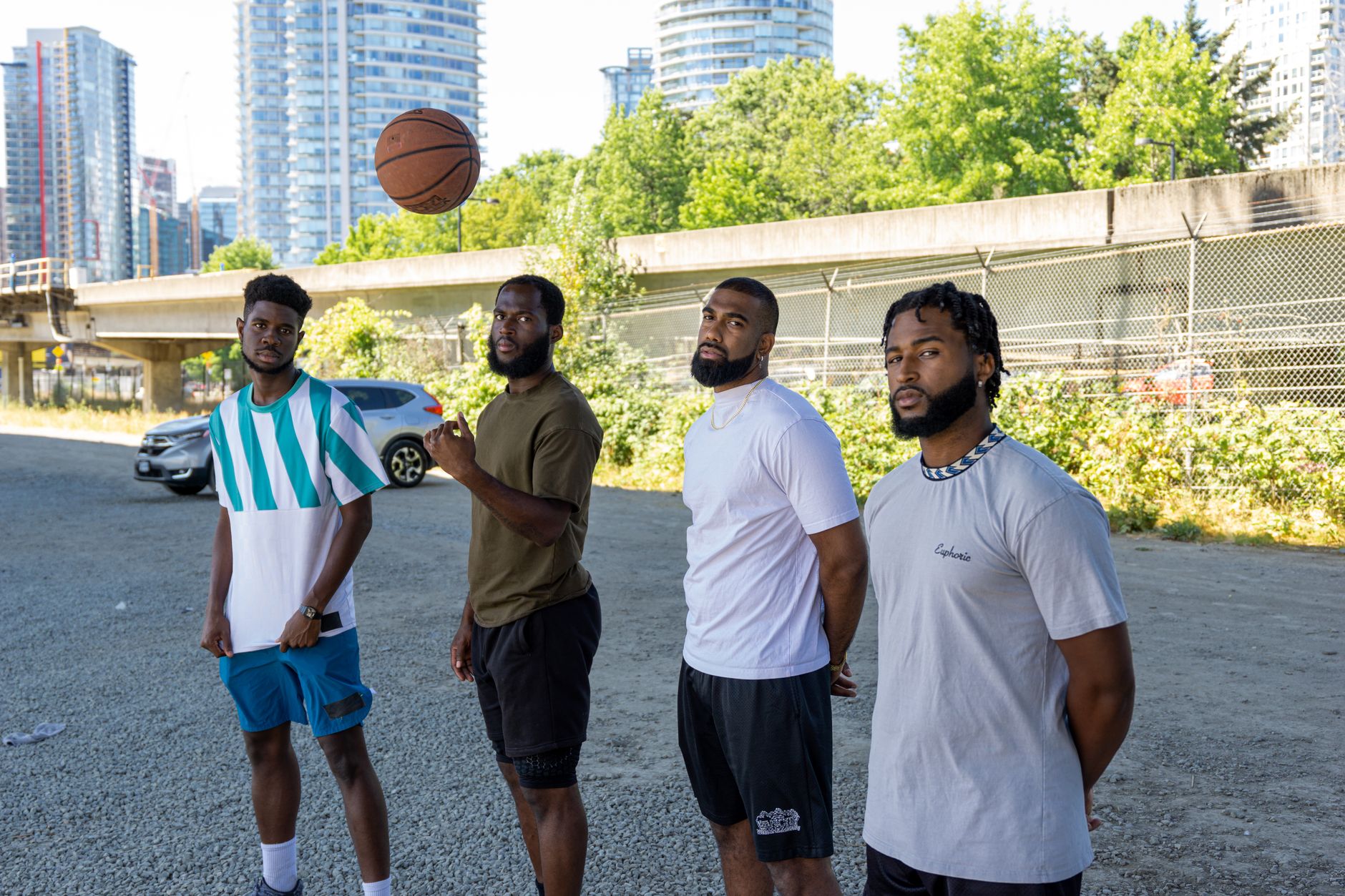 Four young men in sporty casual wear with a basketball, standing in an urban outdoor setting.