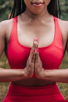 Close-up of a woman in red activewear meditating outdoors with hands in prayer pose.