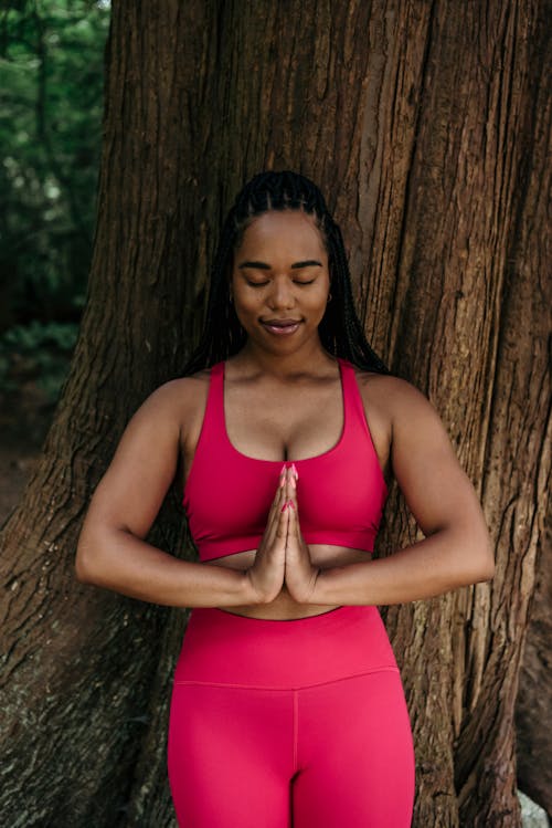 Free Woman in Pink Activewear Standing Beside a Tree Trunk Stock Photo