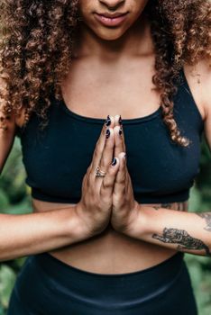 A woman meditating with hands together, wearing a crop top and showcasing arm tattoo.