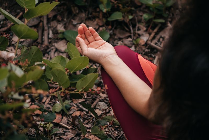 Close-up of a person meditating outdoors surrounded by green leaves