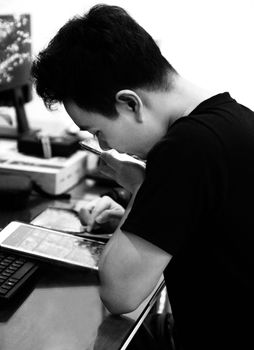 Black and white image of a man concentrating on a tablet at a desk, highlighting focus and technology.