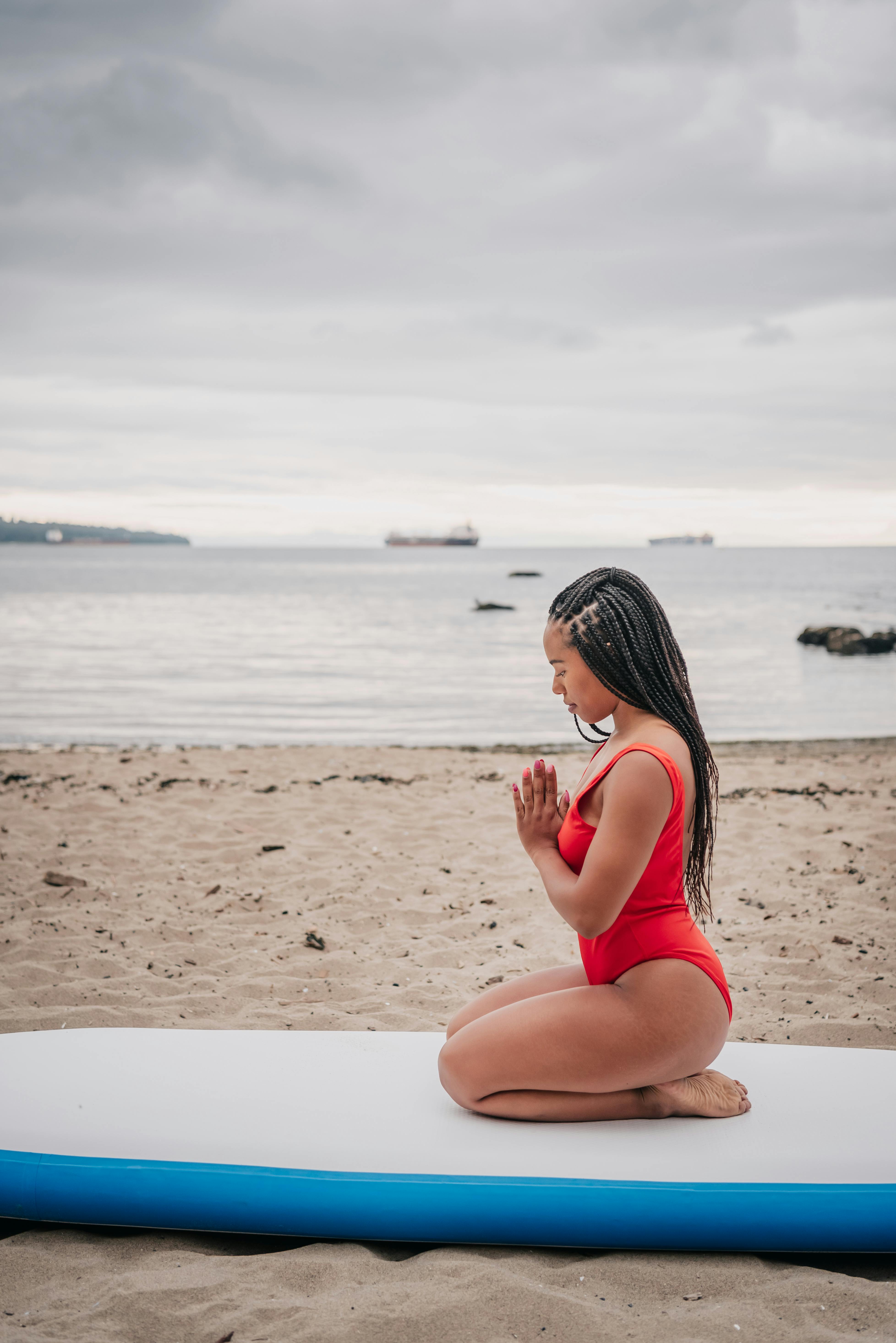 woman in red swimsuit meditating while sitting on a surfboard