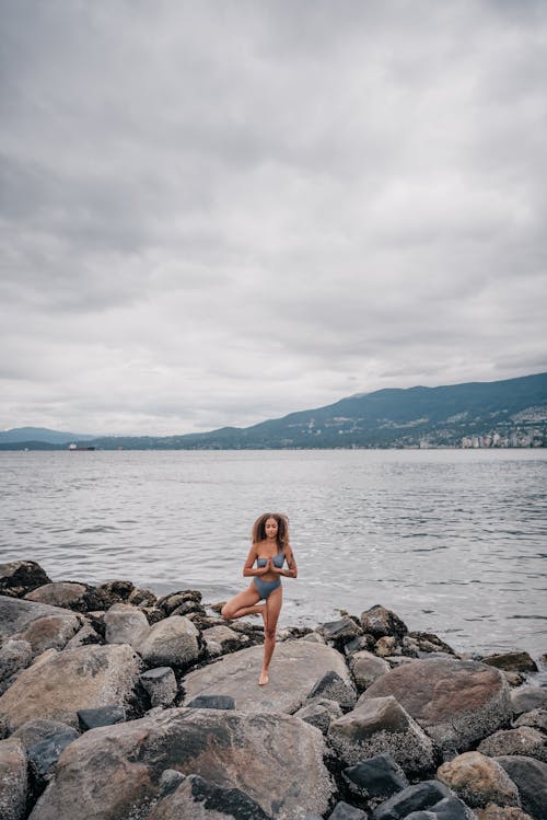 Free Woman in Gray Swimwear Standing on a Rock while Meditating Stock Photo
