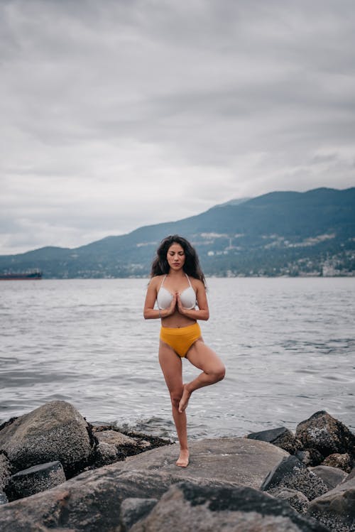 Free Woman in Swimwear Standing on a Rock while Meditating Stock Photo